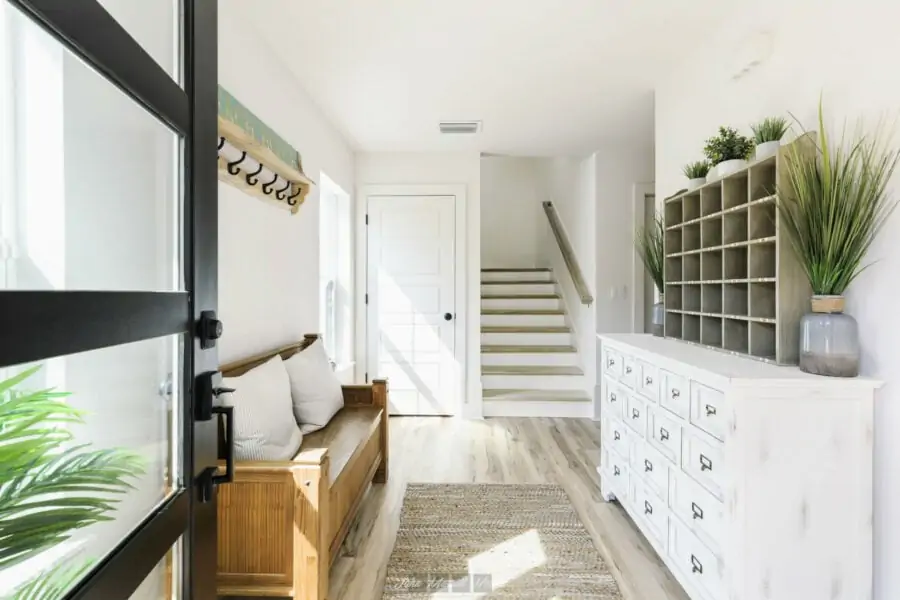 Modern entryway with natural light, wooden furniture, and decorative plants, showcasing a bright, welcoming interior design style by John Merrill Homes.