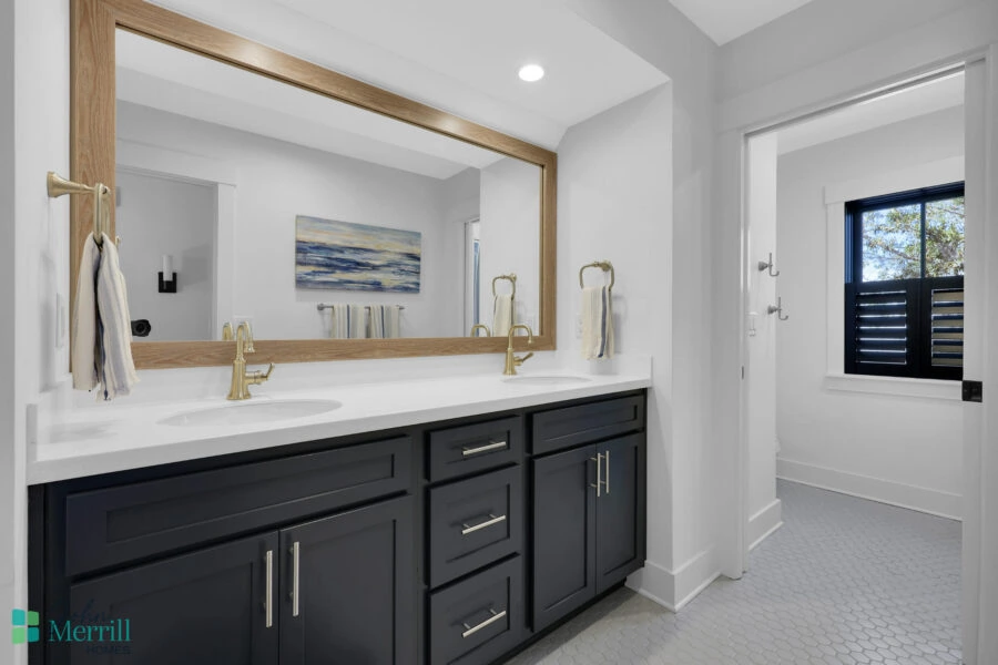 Spacious bathroom featuring a double vanity with dark cabinetry, two gold faucets, and a large wall-mounted mirror, illuminated by recessed lighting, with a window providing natural light.