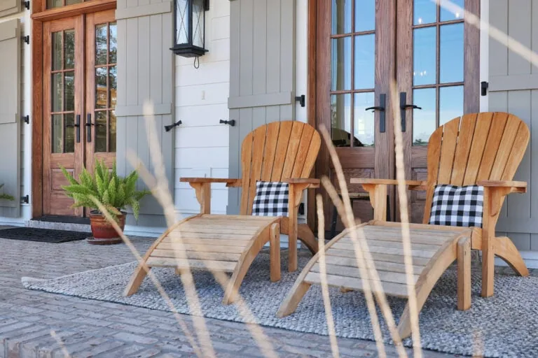Cozy outdoor patio featuring wooden chairs with plaid cushions, a potted plant, and stylish double doors with glass panels, perfect for relaxing and entertaining.