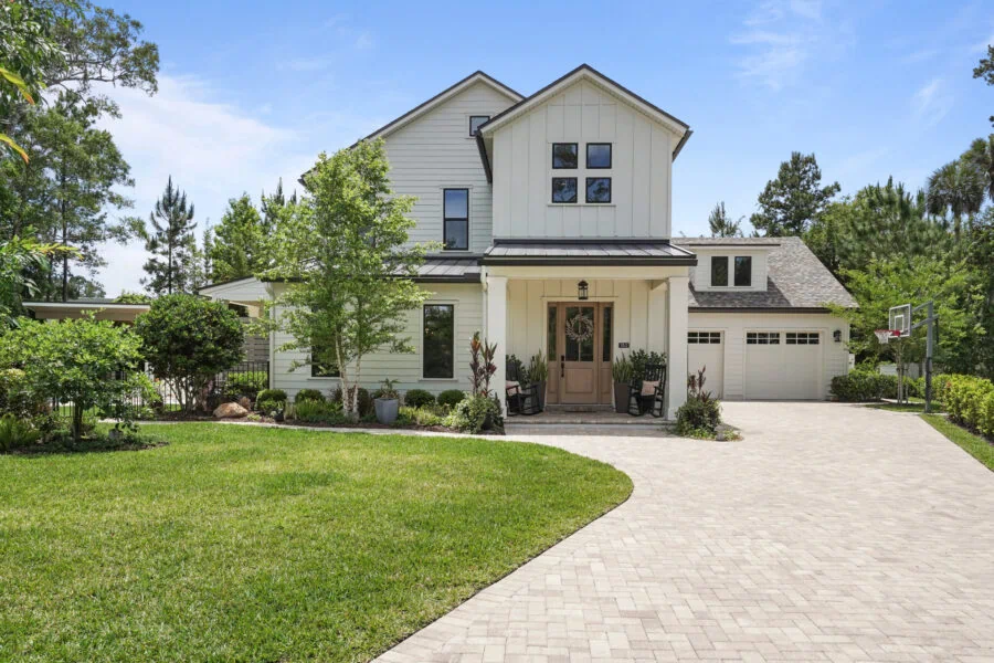 Luxurious modern farmhouse-style home with a well-manicured lawn, paved driveway, and lush landscaping, offering elegant curb appeal and a spacious entrance.