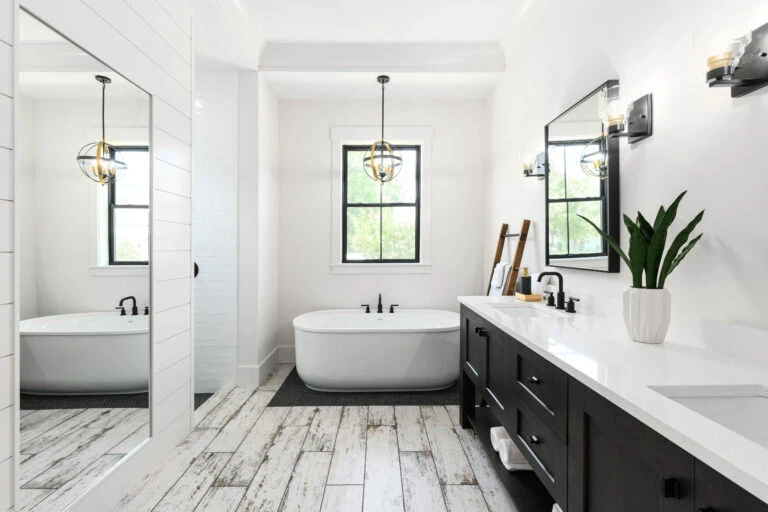 Luxurious modern bathroom featuring a sleek black and white vanity, a stylish freestanding bathtub beneath a large window, and contemporary lighting fixtures for a sophisticated look.