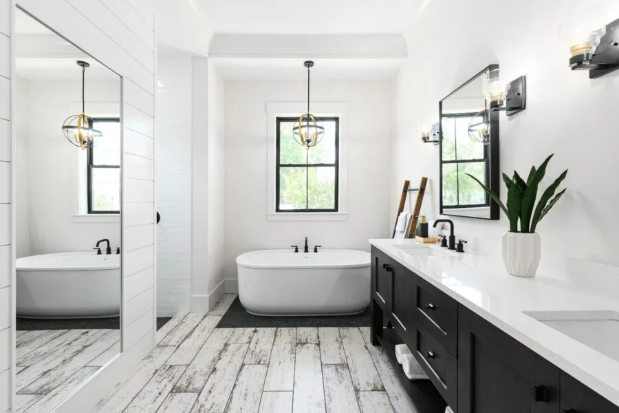 Luxurious modern bathroom featuring a sleek black and white vanity, a stylish freestanding bathtub beneath a large window, and contemporary lighting fixtures for a sophisticated look.