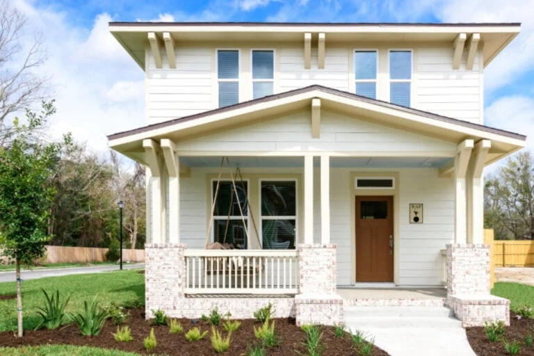 Charming two-story home with a modern design, featuring a welcoming front porch, white siding, and brick accents, surrounded by a well-maintained lawn and landscaping.
