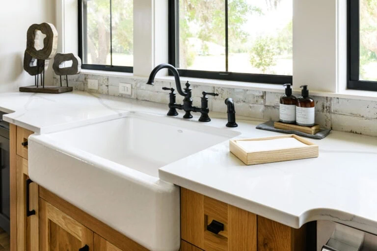 Bright, modern kitchen featuring a farmhouse-style white apron sink with black fixtures, natural wood cabinetry, and large windows that flood the space with natural light, showcasing a contemporary and inviting design.