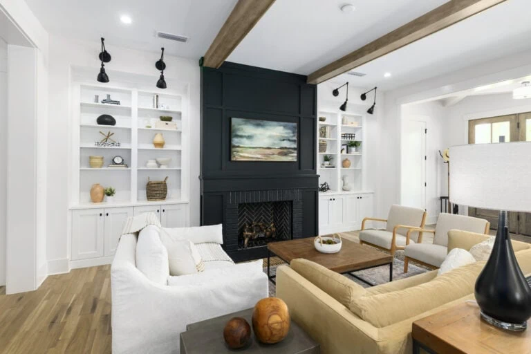 Modern living room with white walls, built-in white bookshelves, a black fireplace, and contemporary furniture including a white sofa and beige armchairs, creating a stylish and inviting space.