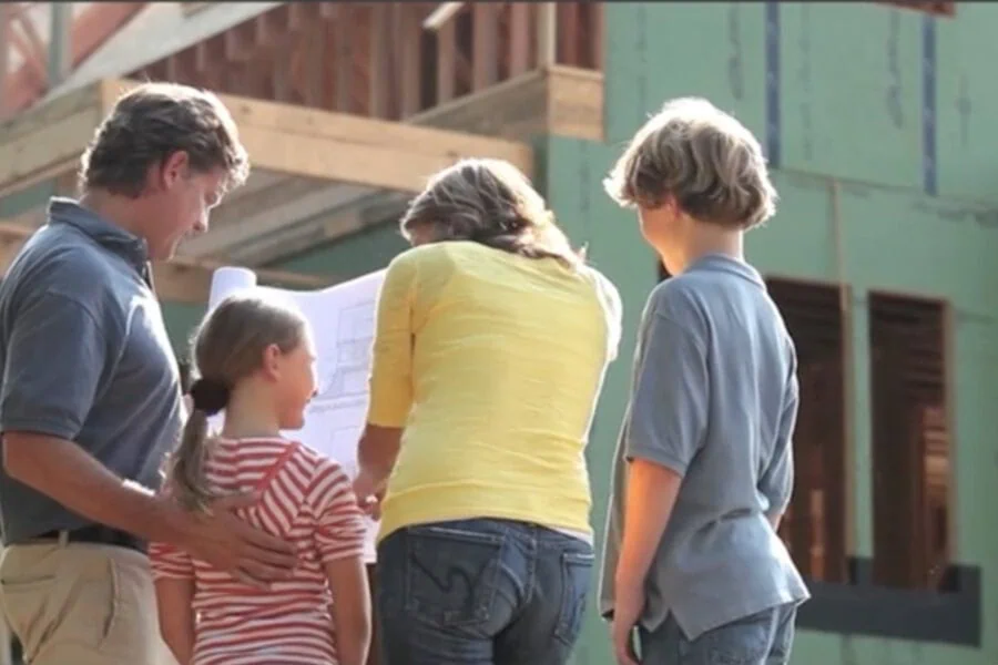 Family discussing blueprints at a new home construction site, representing custom home building services.