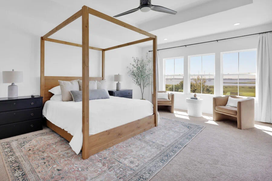Elegant bedroom featuring a modern four-poster wooden bed, stylish black nightstands, comfortable armchairs, and expansive windows showcasing scenic views, creating a bright and inviting space for relaxation and rest.