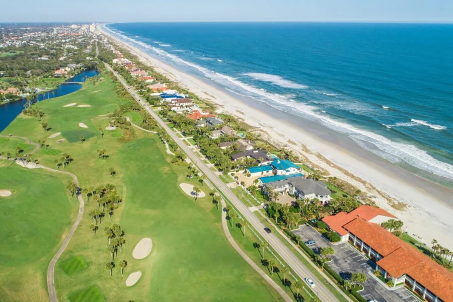 Beachfront homes along a scenic coastline with lush golf courses, palm trees, and scenic water views provide luxurious living near the ocean.
