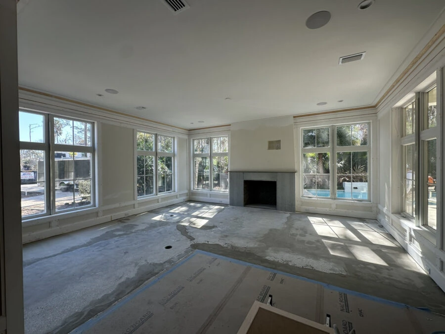 A bright, open-concept living space with multiple large windows allowing natural sunlight to fill the room, showcasing a cozy fireplace and a versatile area for furniture and decor.