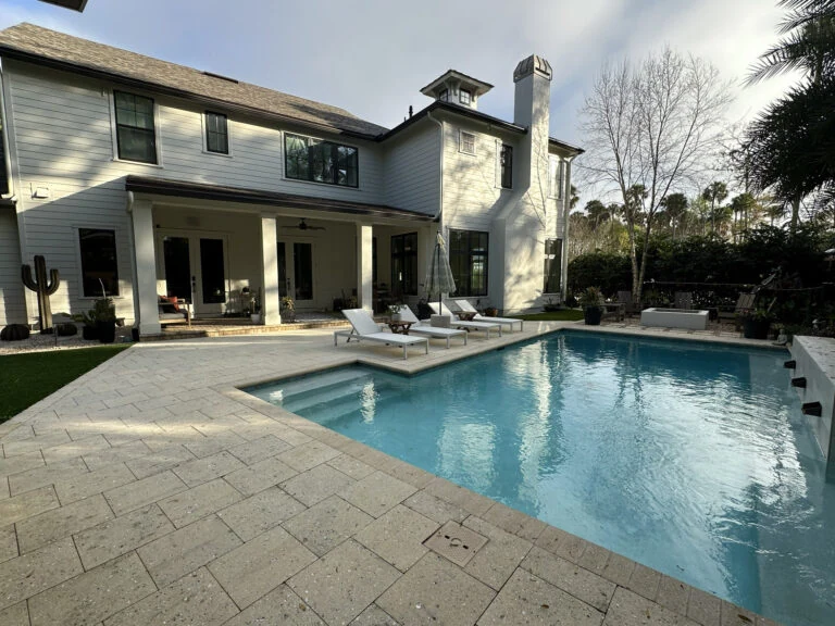 A luxurious two-story house featuring a backyard pool, outdoor seating area, and lush landscaping, perfect for relaxing and entertaining.