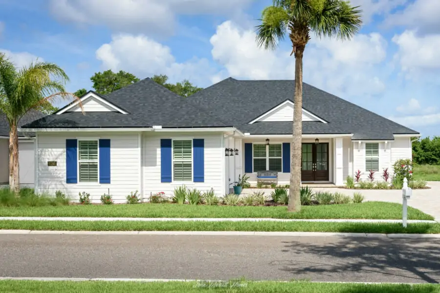 Modern white single-story home with black roof, blue shutters, and lush landscaping, showcasing quality construction and curb appeal.