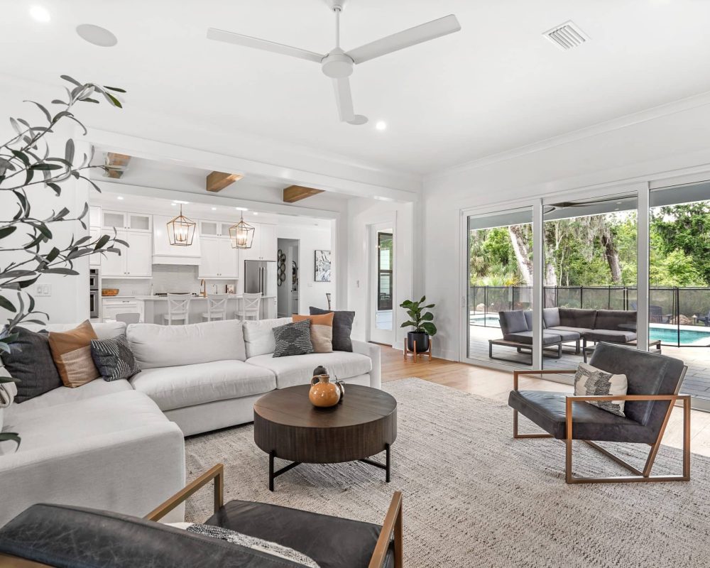 Modern living room interior with white couches, large sliding glass doors leading to outdoor patio and pool, stylish decor, and natural light in a contemporary home.
