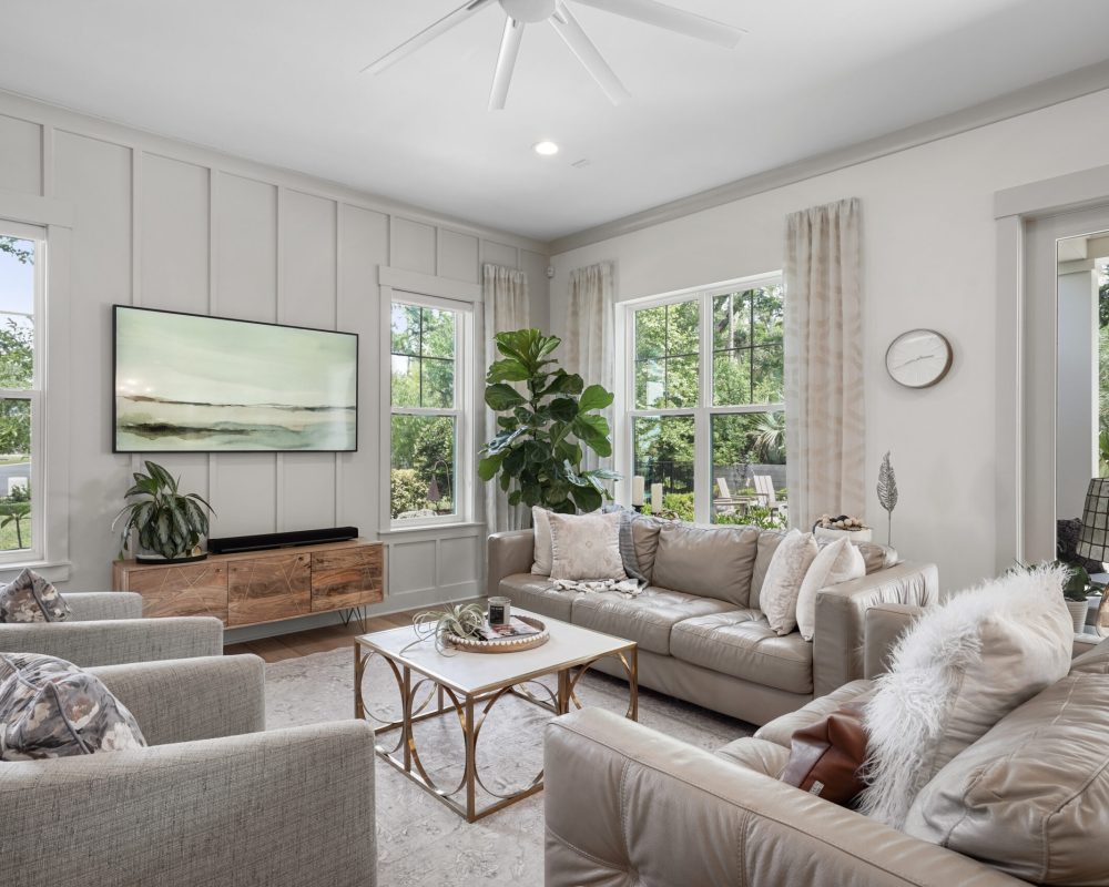 Modern living room with large windows, white walls, cozy beige sofas, and stylish decor, perfect for relaxation and entertaining.