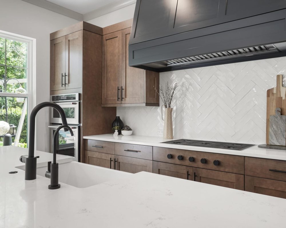 Bright modern kitchen with white quartz countertops, dark wood cabinets, and a white herringbone tile backsplash, featuring a black stove and a large window bringing in natural light.