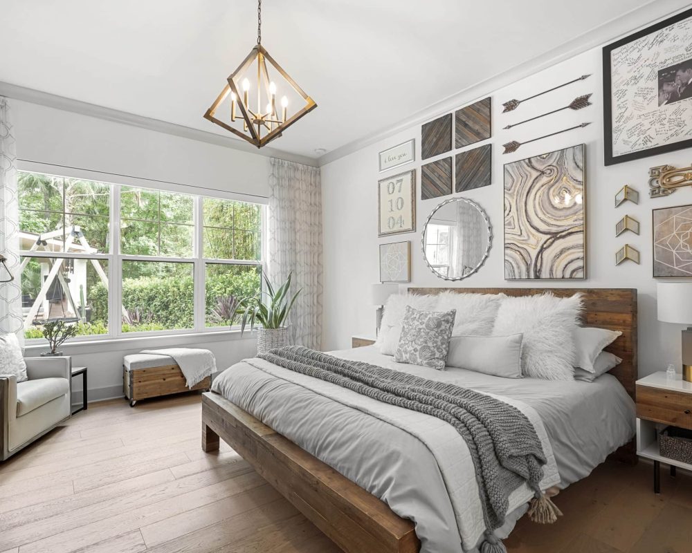 Luxurious master bedroom with a wooden bed frame, contemporary wall art, cozy pillows, and large windows overlooking a lush garden. Modern lighting and elegant decor create a relaxing atmosphere.