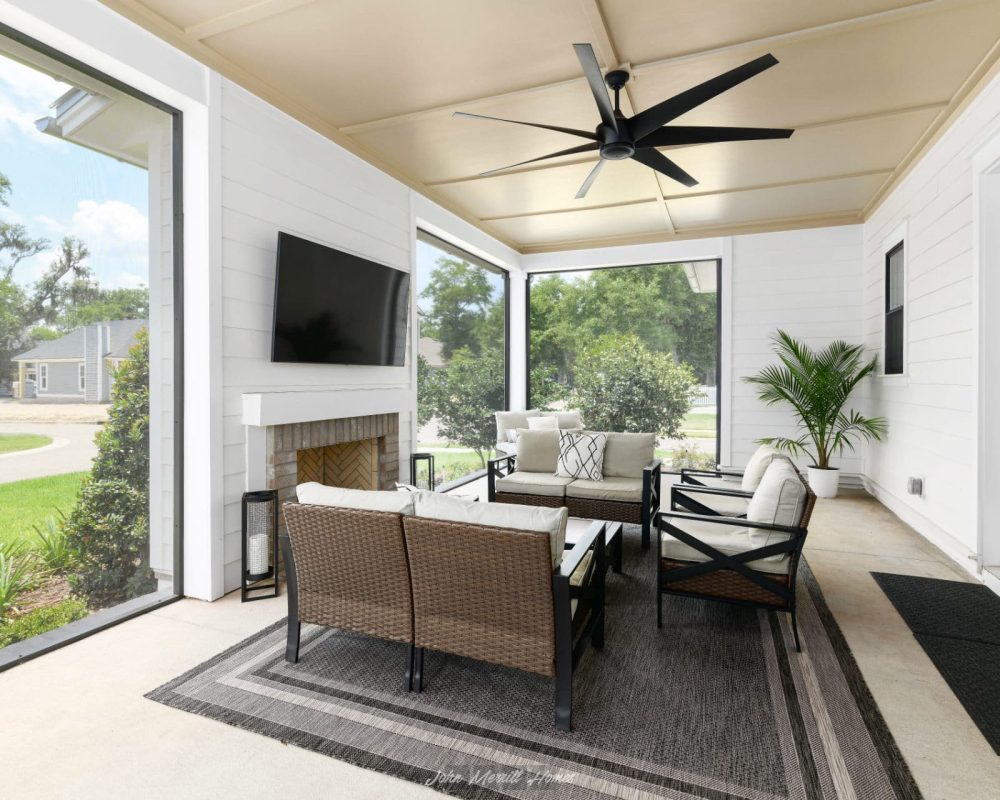 Spacious screened-in porch with comfortable seating, ceiling fan, and fireplace, overlooking lush green yard with trees and neighborhood homes in the background.