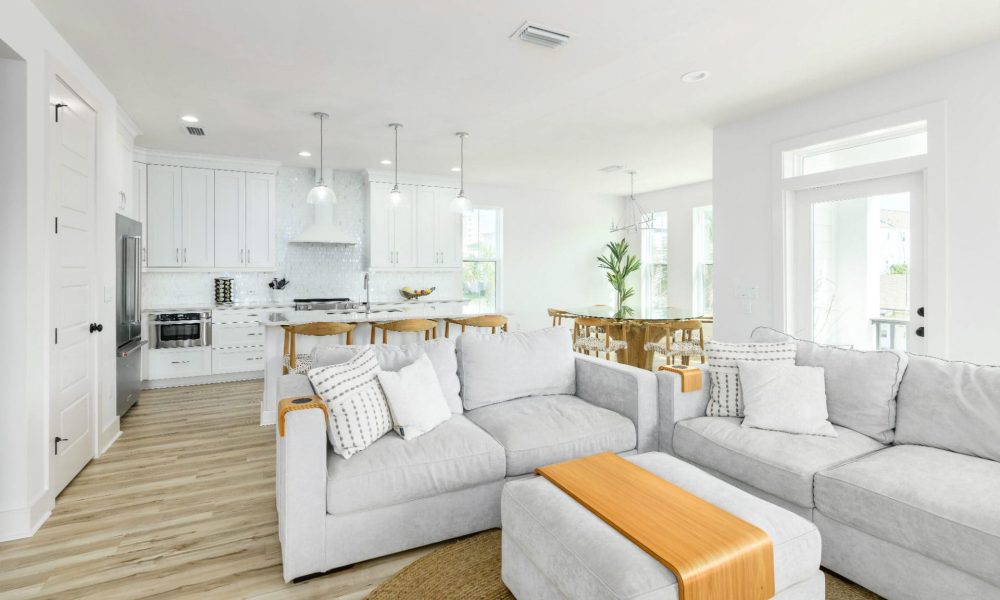 Modern open-concept living room with bright white walls, cozy sectional sofa, and large windows for natural light, seamlessly connected to a stylish kitchen and dining area.