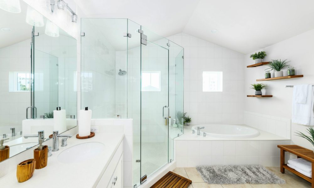 Bright and modern white bathroom featuring a spacious glass-enclosed shower, a built-in bathtub, wooden accents, and stylish wall-mounted shelves with potted plants, creating a relaxing and inviting space.