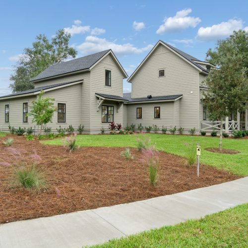1. Modern newly constructed home with gray siding, black window frames, and a landscaped lawn in a suburban neighborhood.