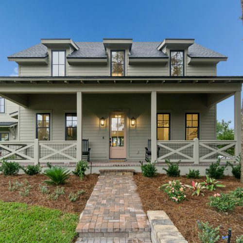Luxurious modern home with a charming front porch, surrounded by lush greenery and colorful flowers, showcasing quality craftsmanship and elegant architectural details.