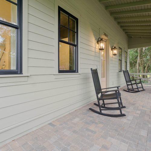 1. Beautiful front porch of a modern American home featuring cozy black rocking chairs, exterior lighting, and a view of lush greenery, perfect for relaxing outdoors.