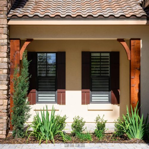 Elegant front porch of a modern home featuring stone and stucco exterior, wooden accents, black shutters, outdoor lanterns, and well-maintained landscaping.