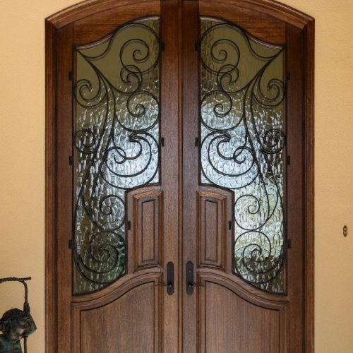 Elegant wooden front door with ornate wrought iron detailing, setting a welcoming tone for a beautiful home.