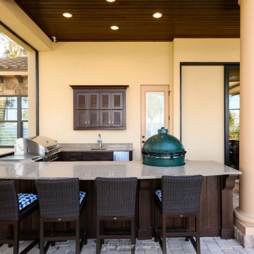 Outdoor kitchen with granite countertops, built-in grill, seating area, and stylish cabinetry, perfect for entertaining in a modern home.