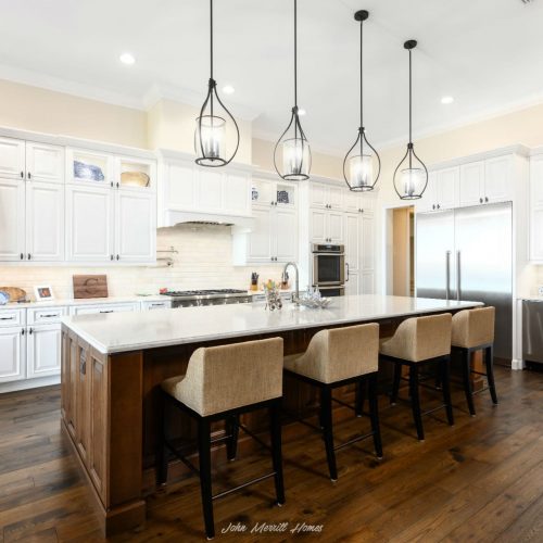 Bright white kitchen with a large island, elegant pendant lighting, and stainless steel appliances, featuring a cozy and modern design perfect for family cooking and entertaining.