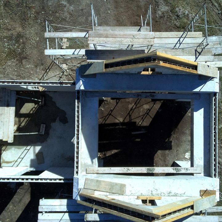 Constructing a modern residential building with a steel frame structure on a hillside, featuring multiple levels and safety railings, in an early stage of development.
