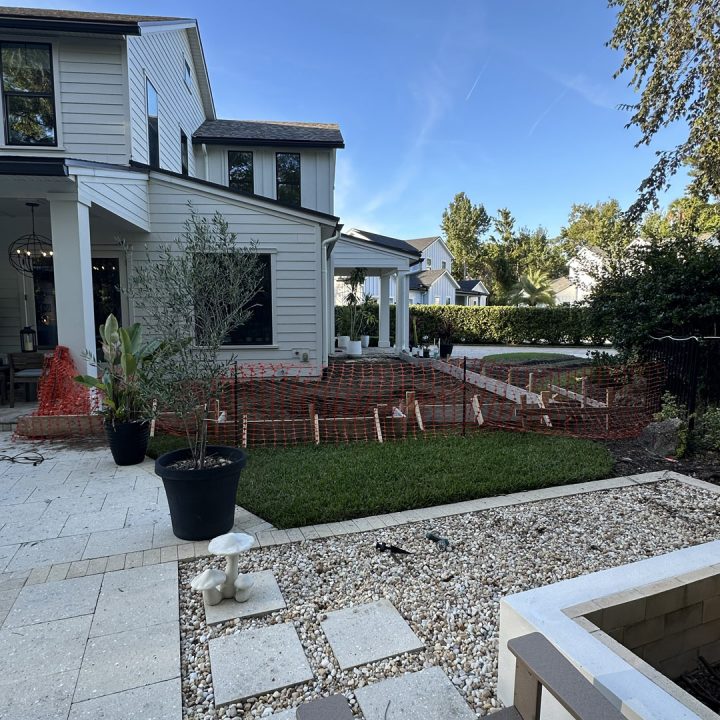Modern two-story white house with a landscaped backyard, potted plants, and a stone pathway under a clear blue sky.
