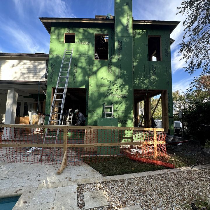 New green house under construction with scaffolding and ladders, surrounded by trees and a partly cloudy sky.