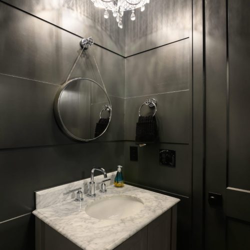Luxurious black bathroom featuring a marble countertop, round mirror, and ornate chandelier lighting for a sophisticated ambiance.