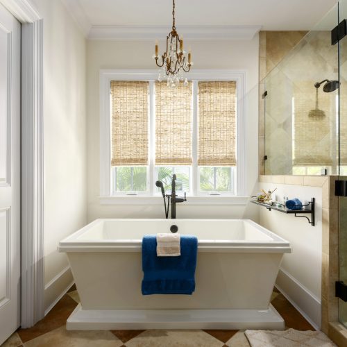 Elegant bathroom featuring a freestanding bathtub and a spacious walk-in shower with glass enclosure. Natural light fills the room through large windows with woven shades.