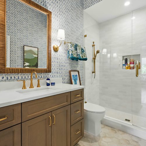 Bathroom with walk-in shower, gold fixtures, and patterned wallpaper.