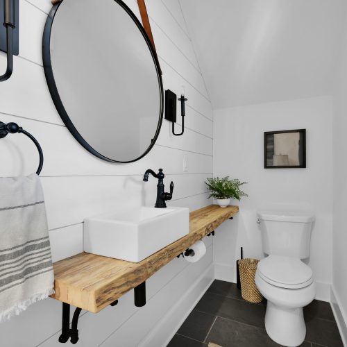 Bathroom with white shiplap walls, black fixtures, a wooden vanity with a vessel sink, and a toilet, creating a clean and stylish space.