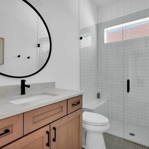 Bright bathroom featuring a large mirror, white tiled walls, and a walk-in shower with black fixtures.
