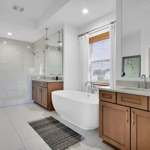 Spacious bathroom featuring a sleek freestanding bathtub, a large walk-in shower with glass doors, and elegant wooden cabinetry under a bright window.