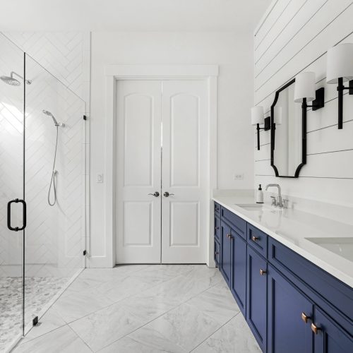 Bright and spacious bathroom featuring a sleek glass-enclosed shower, white walls, and a stylish blue double vanity with modern fixtures.