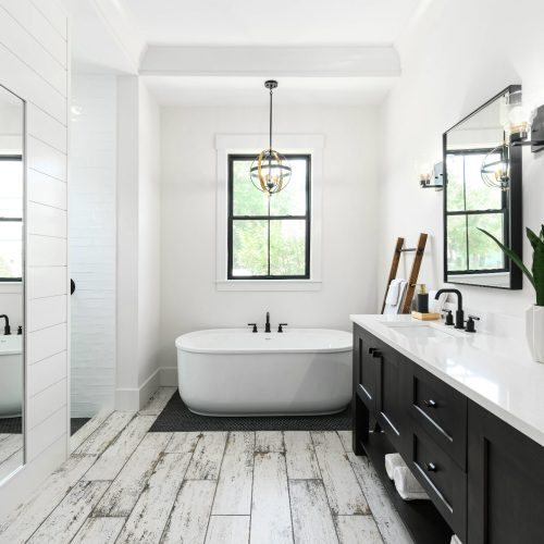 Bright and spacious bathroom featuring a sleek freestanding bathtub, large windows providing natural light, and a stylish double vanity with black cabinets and white countertop.