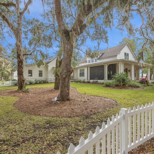 A charming house surrounded by mature trees and a white picket fence, featuring a spacious yard and well-maintained landscaping, ideal for family living and outdoor activities.