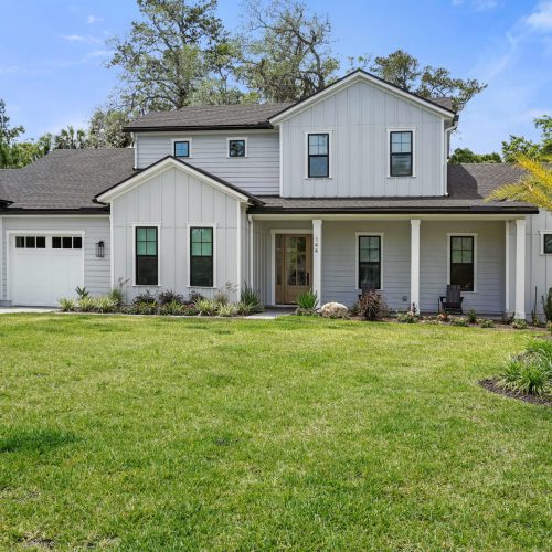 Beautiful modern farmhouse with white exterior, large front yard, and landscaped garden, featuring a two-story design and attached garage.