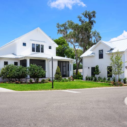 Beautiful white two-story houses with well-maintained lawns, surrounded by greenery and trees, showcasing contemporary residential architecture.