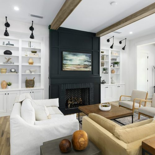 A welcoming living room featuring a central fireplace with a black surround, surrounded by white built-in shelves filled with decorative items, and furnished with beige and white sofas and armchairs.