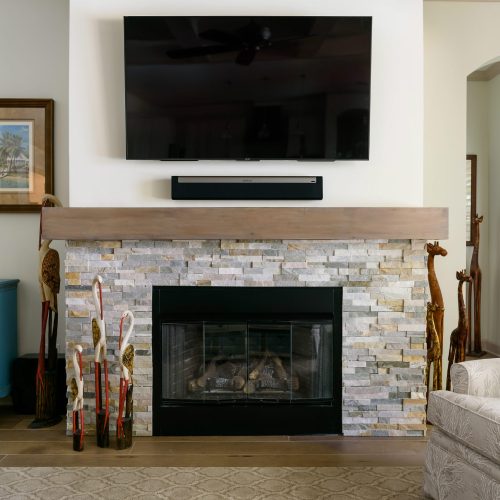 A modern living room featuring a stone fireplace with a mounted flat-screen TV above, complemented by a blue side table and comfortable beige sofa.