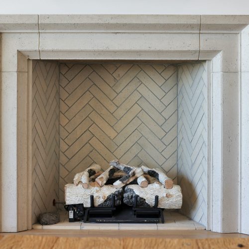 A modern fireplace featuring a clean, beige stone surround and a neatly arranged stack of decorative logs inside. The fireplace adds warmth and style to the living space.