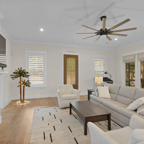 Spacious living room featuring a cozy fireplace, large windows with natural light, and comfortable seating including a sofa and armchairs, perfect for relaxing or entertaining guests.