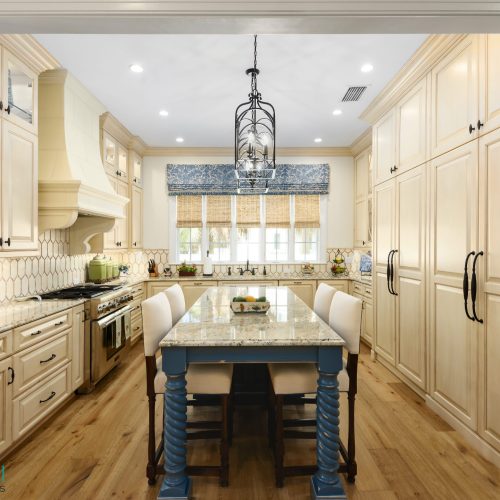 Bright and inviting kitchen featuring cream-colored cabinetry, a central island with blue legs, and a large window with a blue valance providing natural light.