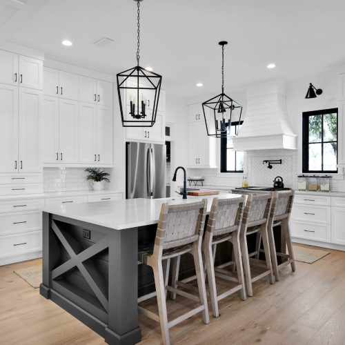 Modern white kitchen featuring a large island with seating, pendant lighting, and sleek cabinetry. Bright, airy space ideal for cooking and entertaining.