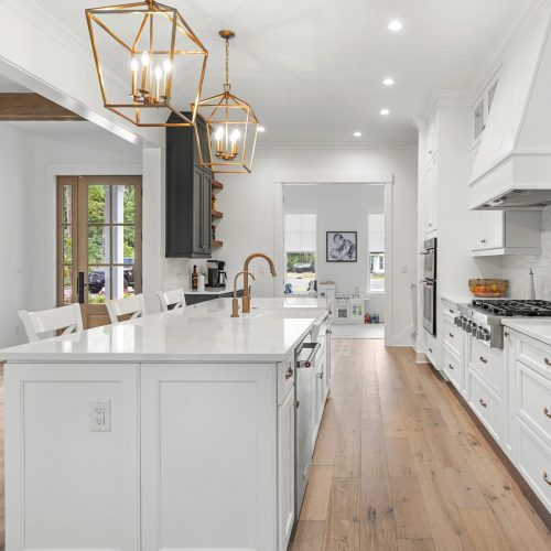 A bright, modern kitchen featuring white cabinetry, a large island with a sink, stainless steel refrigerator, and elegant pendant lighting, perfect for contemporary home living.